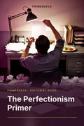 PrimerDeck cover: The Perfectionism Primer: man examines a single page under a desk lamp, crumpled drafts scattered around him